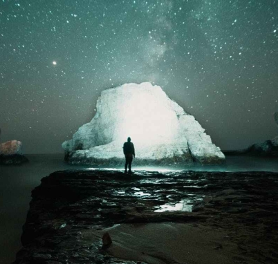 person standing on rock formation near body of water during night time